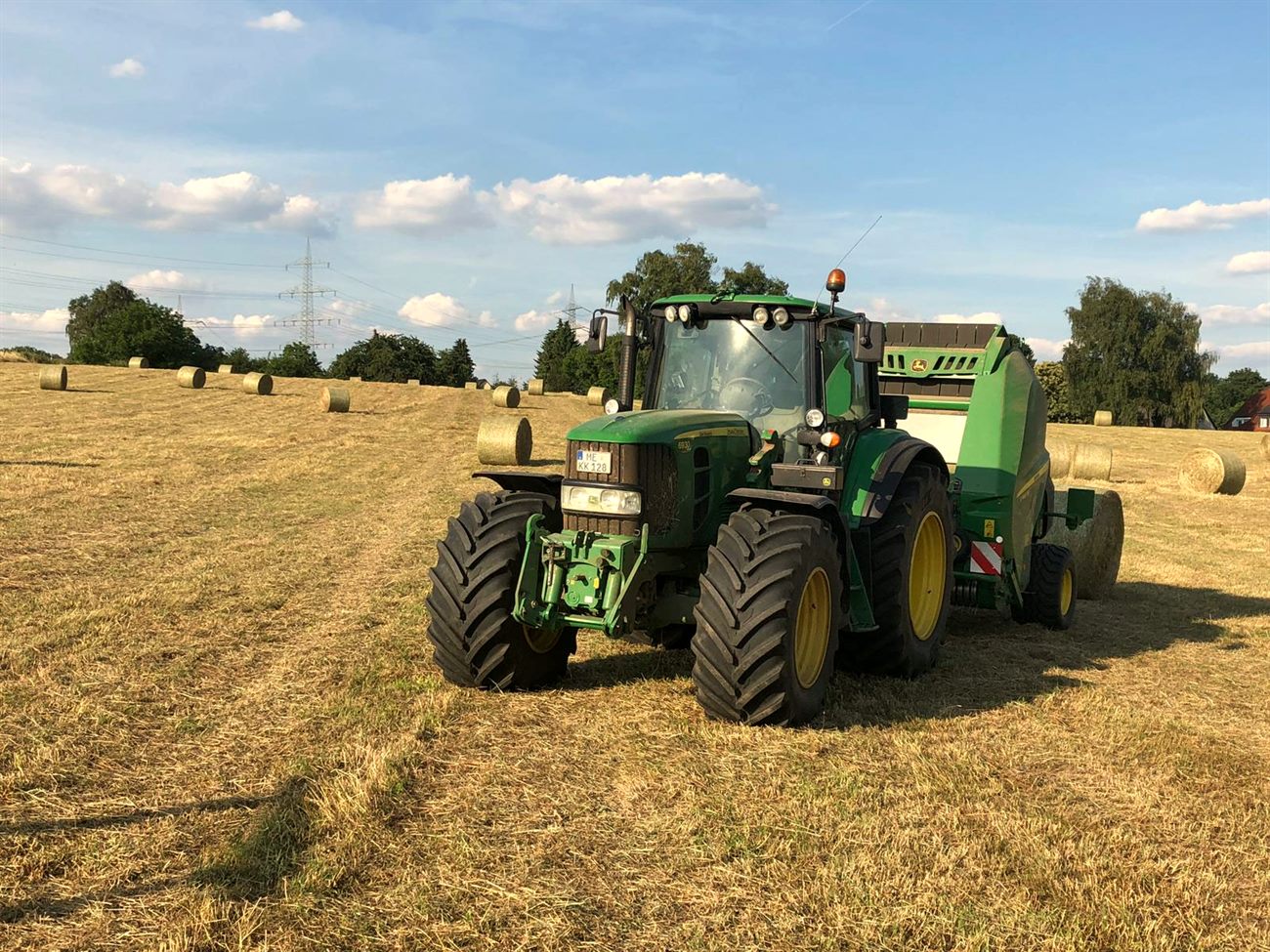 Eigene Landwirtschaft: Traktor mit Ballenpresse bei der Heuernte auf den Feldern des Hofes